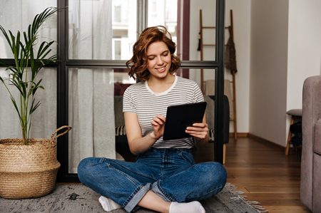 Young girl in comfortable clothes with smile looks into tablet and poses in living room