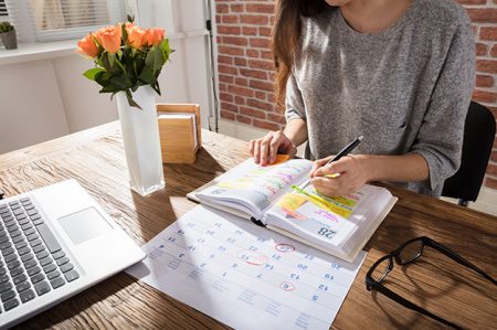 Close-up Of A Businesswoman Making Agenda On Personal Organizer At Workplace